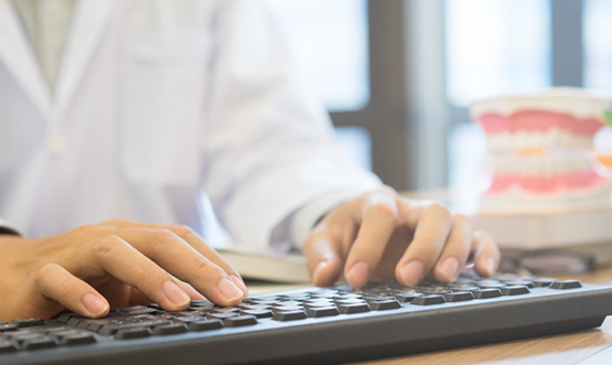 Hands typing on keyboard at dental office desk with blurred background