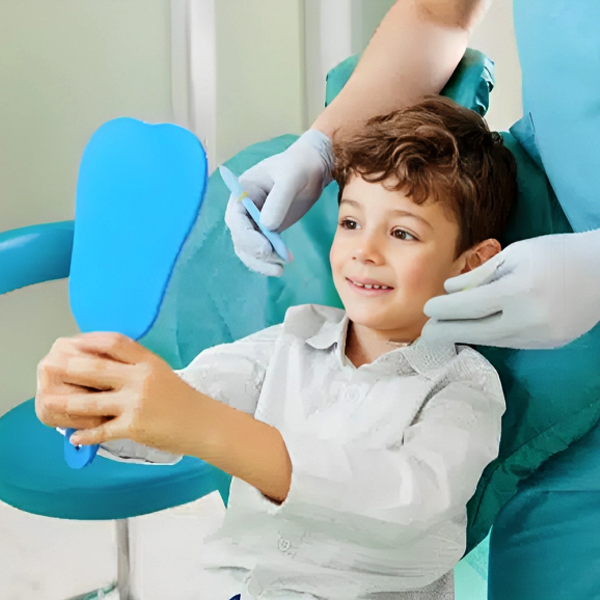 Young boy smiling while holding blue mirror in pediatric dental office with dentist.