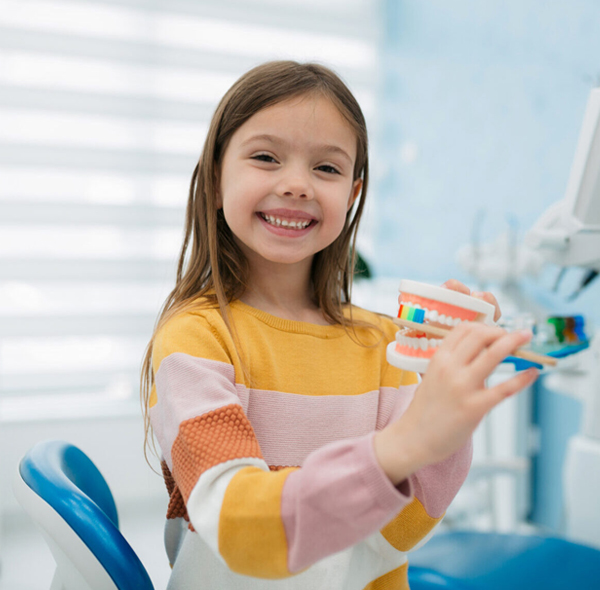 Young girl smiling while holding colorful toothbrushes in bright dental office setting.