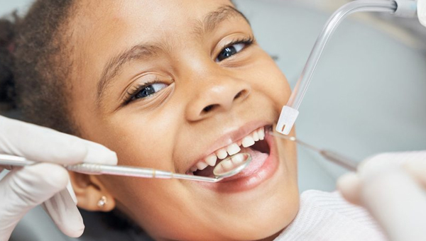 Young child smiling during dental examination with dentist's tools in bright clinical setting.