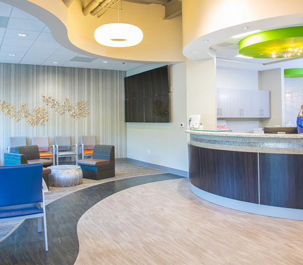Modern pediatric dental office reception area with comfortable seating and curved service desk