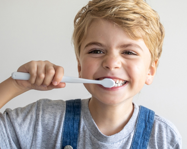 Young boy brushing teeth with toothbrush, smiling against white background.