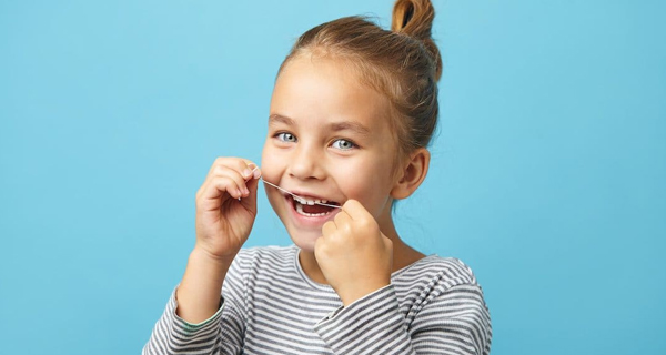 Young girl smiling brightly while flossing teeth against blue background.