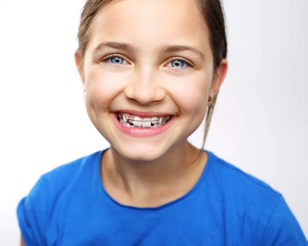 Smiling child in blue shirt displays healthy teeth against white background for pediatric dental practice.