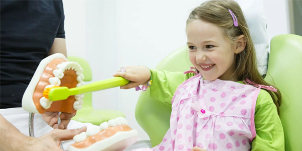 Young girl in green shirt smiling while holding colorful toy at pediatric dental office visit.