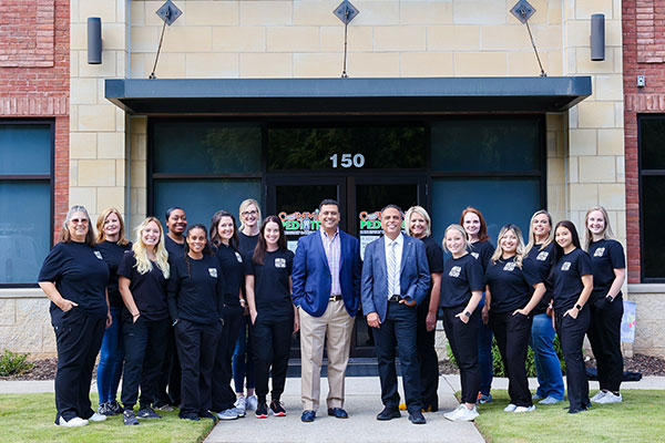 Cumming Pediatric Dentistry & Orthodontics team members posing together outside brick building entrance.