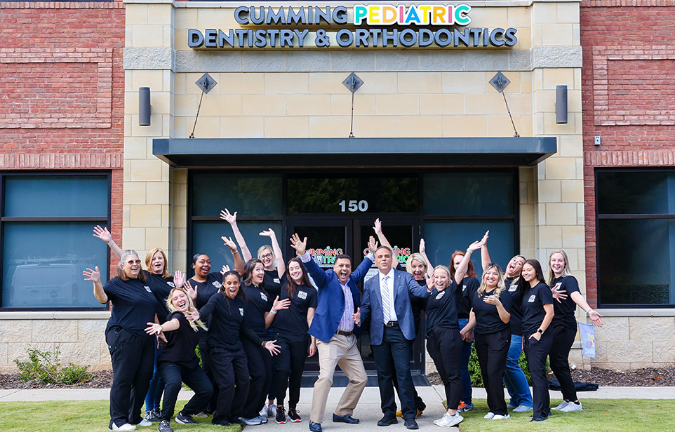 Team of dental professionals posing together outside Cumming Pediatric Dentistry & Orthodontics office building.
