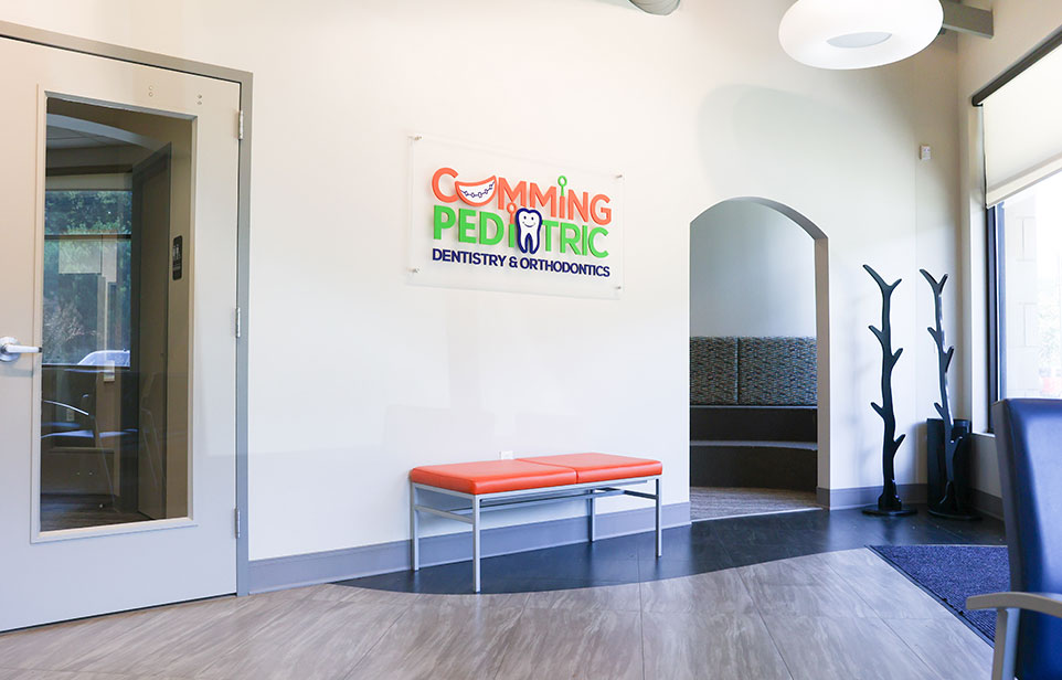 Modern pediatric dental office waiting room with colorful signage, bench seating, and glass door entrance.