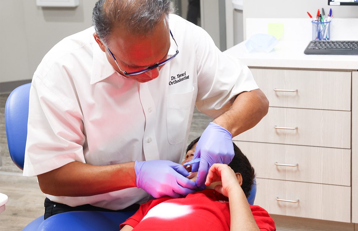 Pediatric dentist in pink shirt examines young patient's teeth in dental office treatment room.